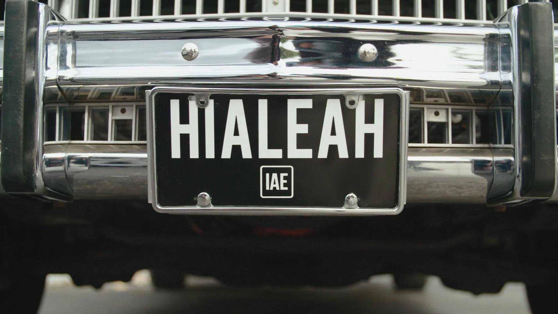 Close-up of a black front license plate that reads 'HIALEAH' on a shiny chrome vehicle bumper.