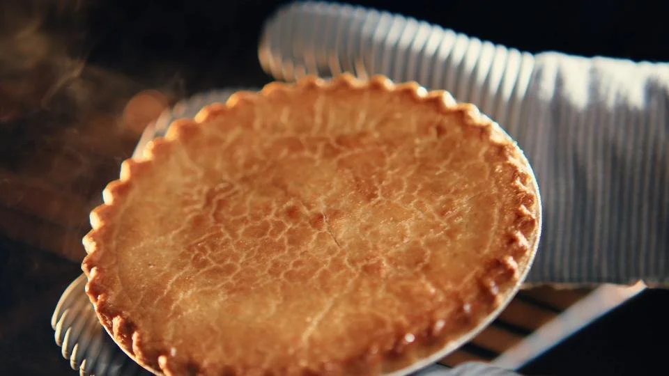 A freshly baked pie with a golden crust held over a ceramic plate.