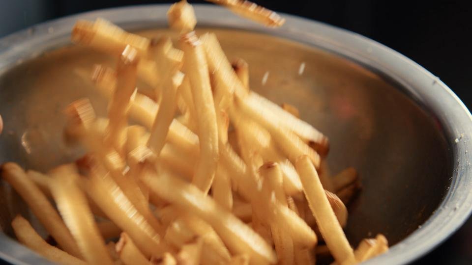 French fries being poured into a metal bowl.