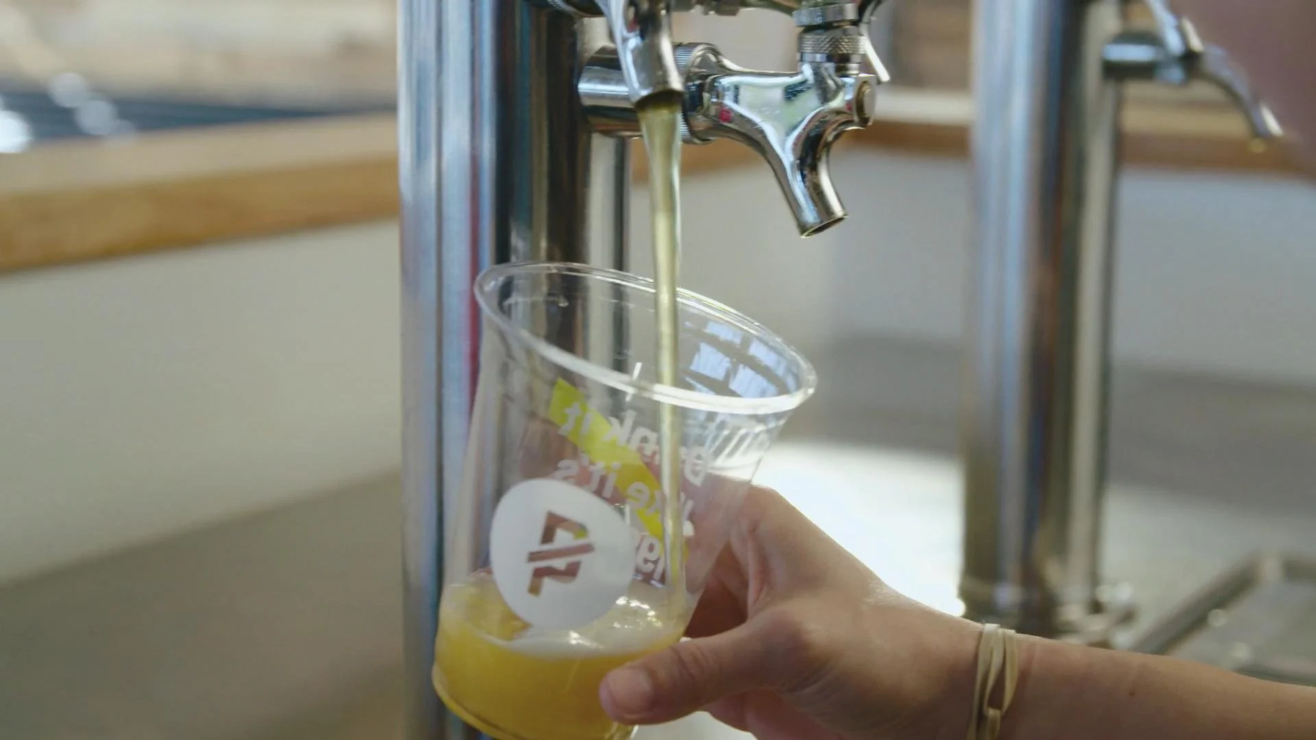 Person filling a clear plastic cup with yellow liquid from a water fountain