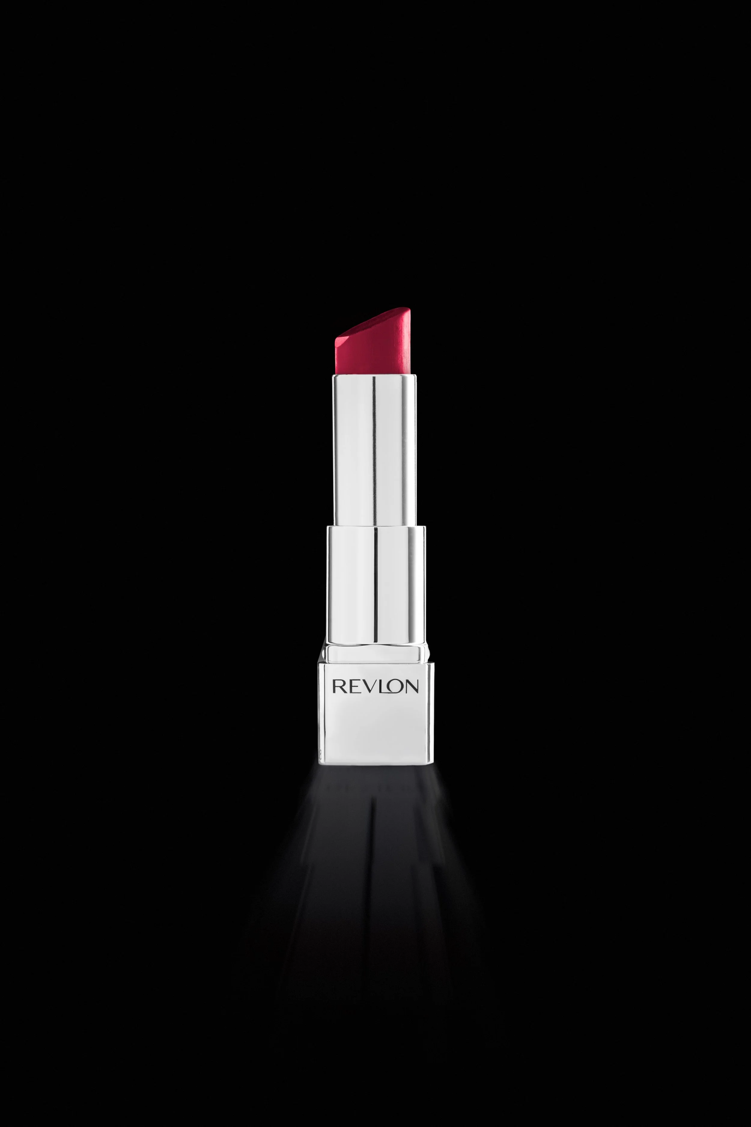 A tube of Revlon lipstick with a silver and white case, standing upright against a black background, casting a reflection.