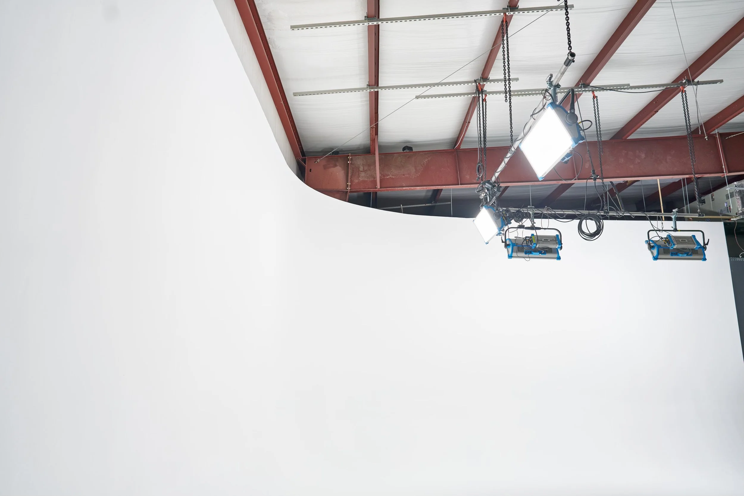Lighting equipment installed on a ceiling with exposed red steel beams and white walls.