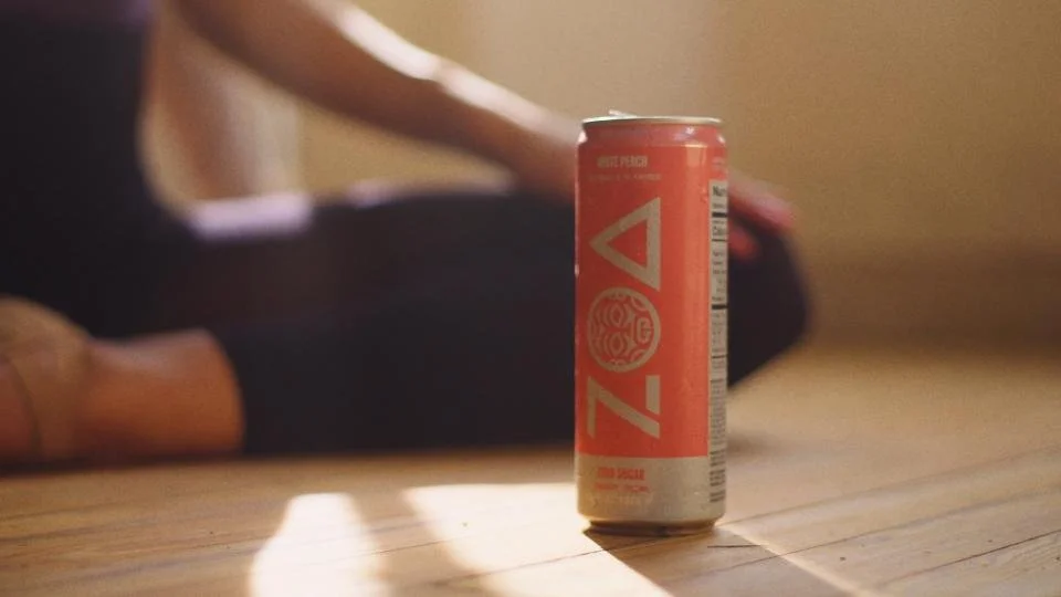 A can of Zevia soda placed on a wooden floor with a person sitting on the floor in the background.