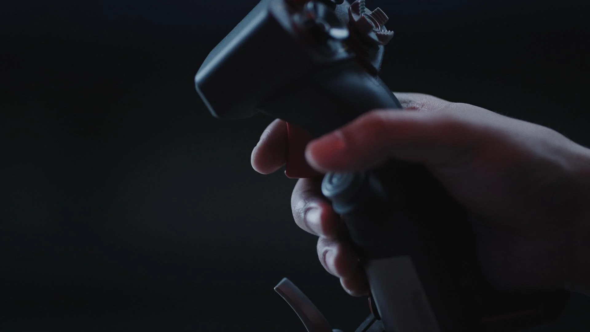 A hand holding a remote control in a dark setting.