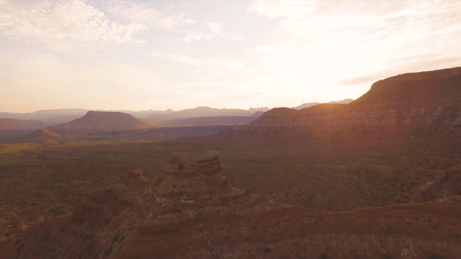 A desert landscape at sunset with layered mesas and canyon formations under a partly cloudy sky.