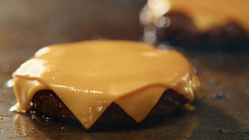 Close-up of a cheeseburger patty topped with melted cheese on a flat surface.