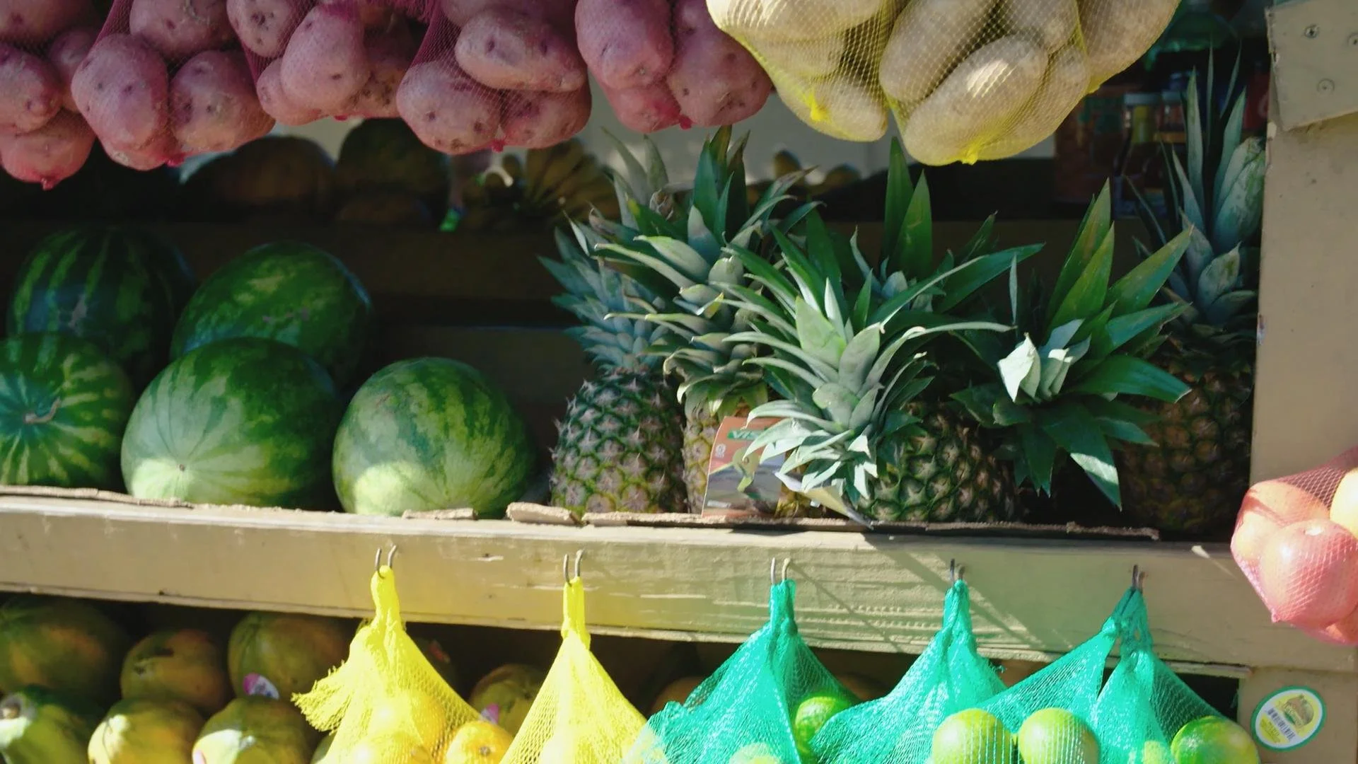 Display of fresh produce including watermelons, pineapples, and onions on market shelves.