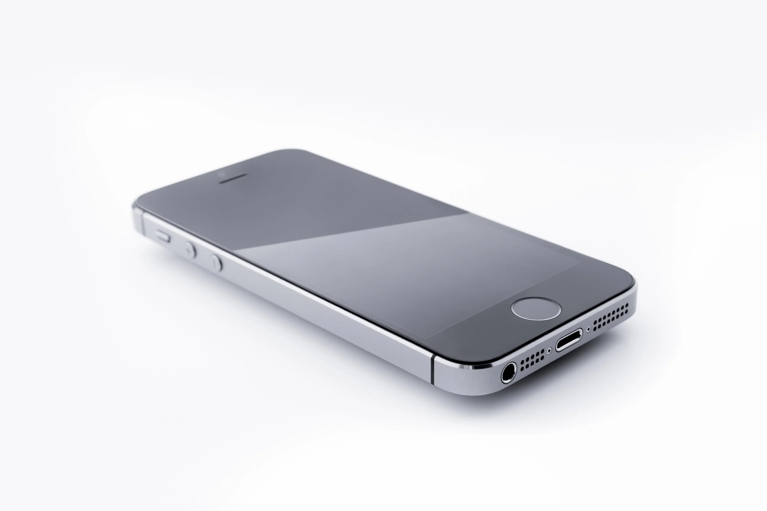 Silver smartphone lying flat on a white surface, showing the bottom edge with speaker and charging port.