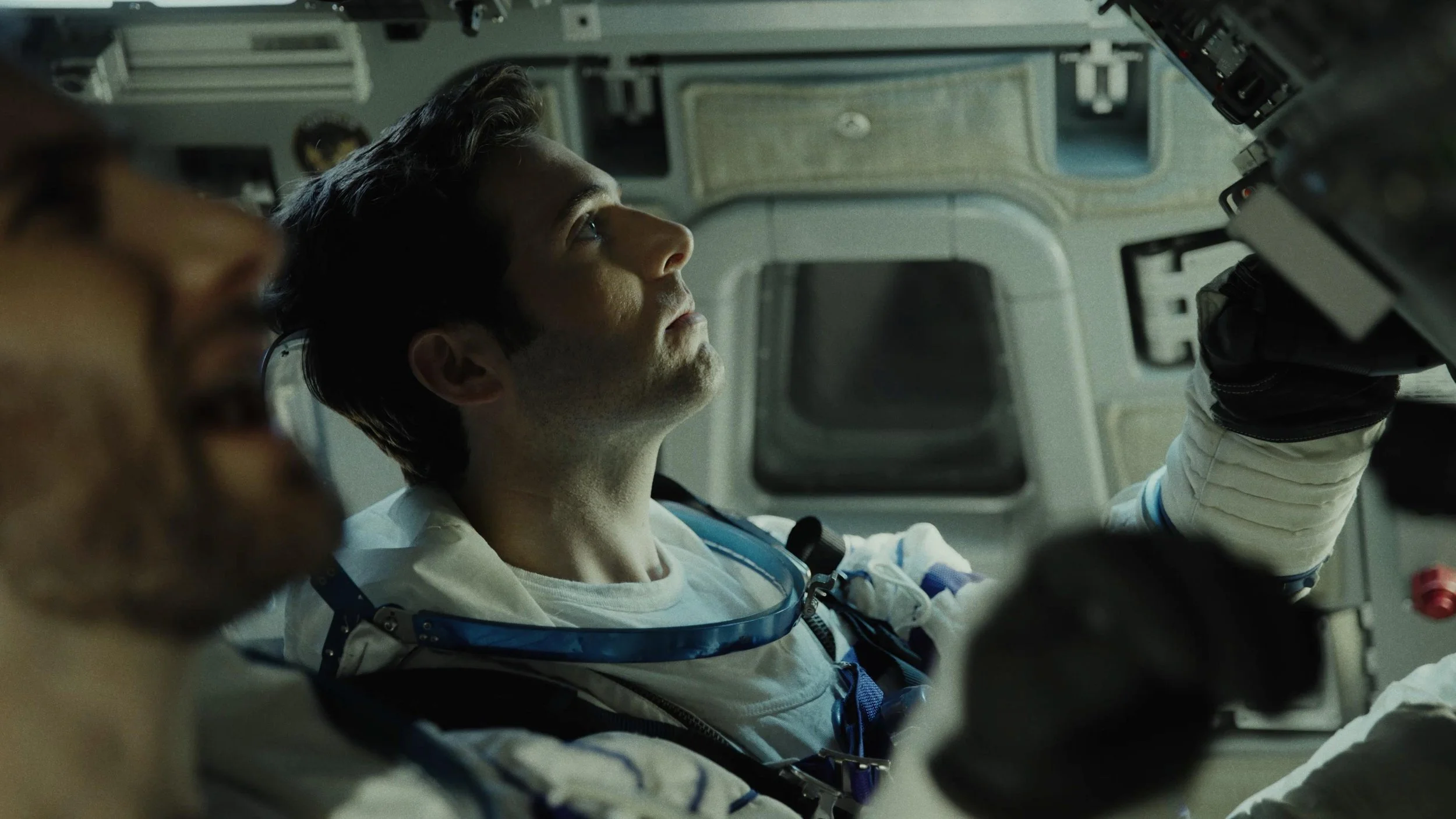An astronaut inside a spacecraft, looking upwards while floating in space with other crew members visible nearby.