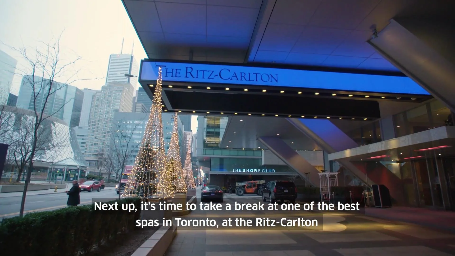 Exterior view of The Ritz-Carlton hotel in Toronto during daytime with Christmas decorations, including lit-up trees, and city skyscrapers in the background.