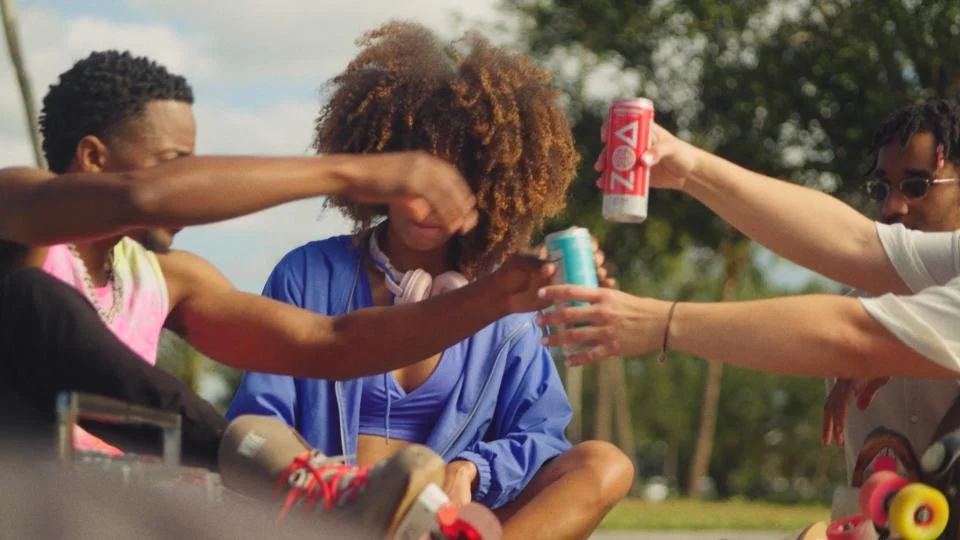 Group of young friends outdoors, sitting together, passing drinks, smiling and having fun.
