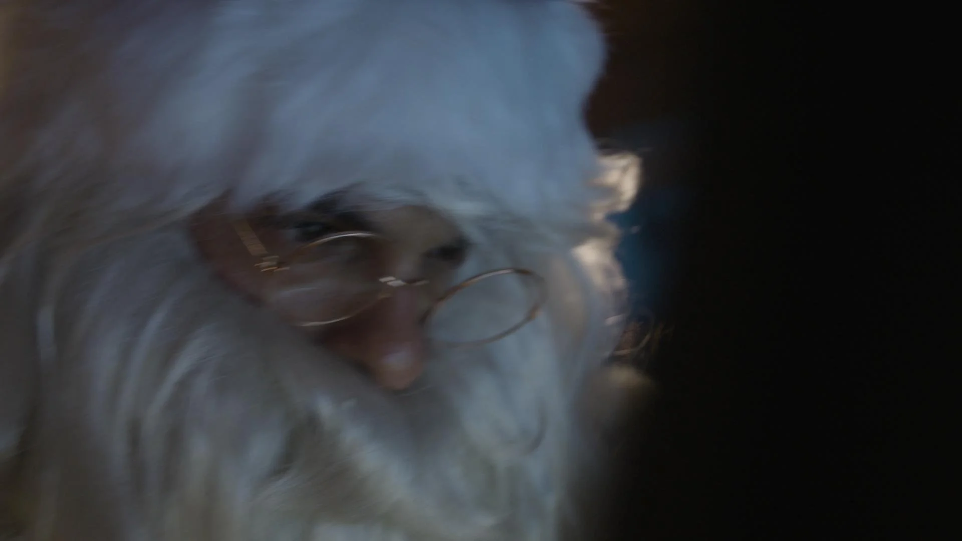 Close-up of a person with long, light-colored hair, wearing glasses, with a dark background.
