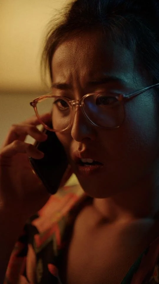 A young woman with glasses talking on a cell phone, showing a worried or confused expression.