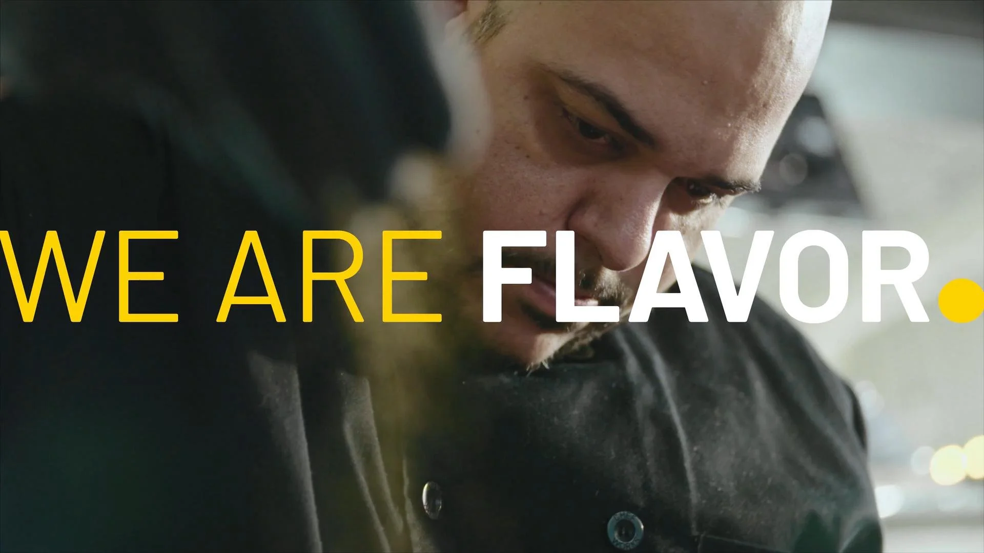 Close-up of a man's face with a focused expression, overlaid with the text 'WE ARE FLAVOR' in bold yellow and white letters.