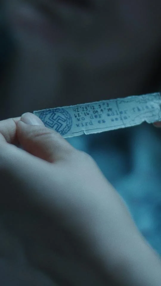 Person holding a torn paper with a blue ink stamp of a swastika and German text.