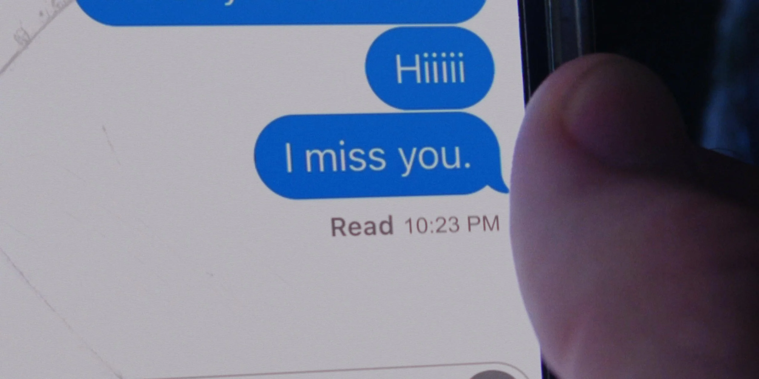 Text message conversation on a phone screen showing the message 'Hiiiii' followed by 'I miss you.' with a timestamp "Read 10:23 PM". A person's finger is partially visible near the right side of the screen.