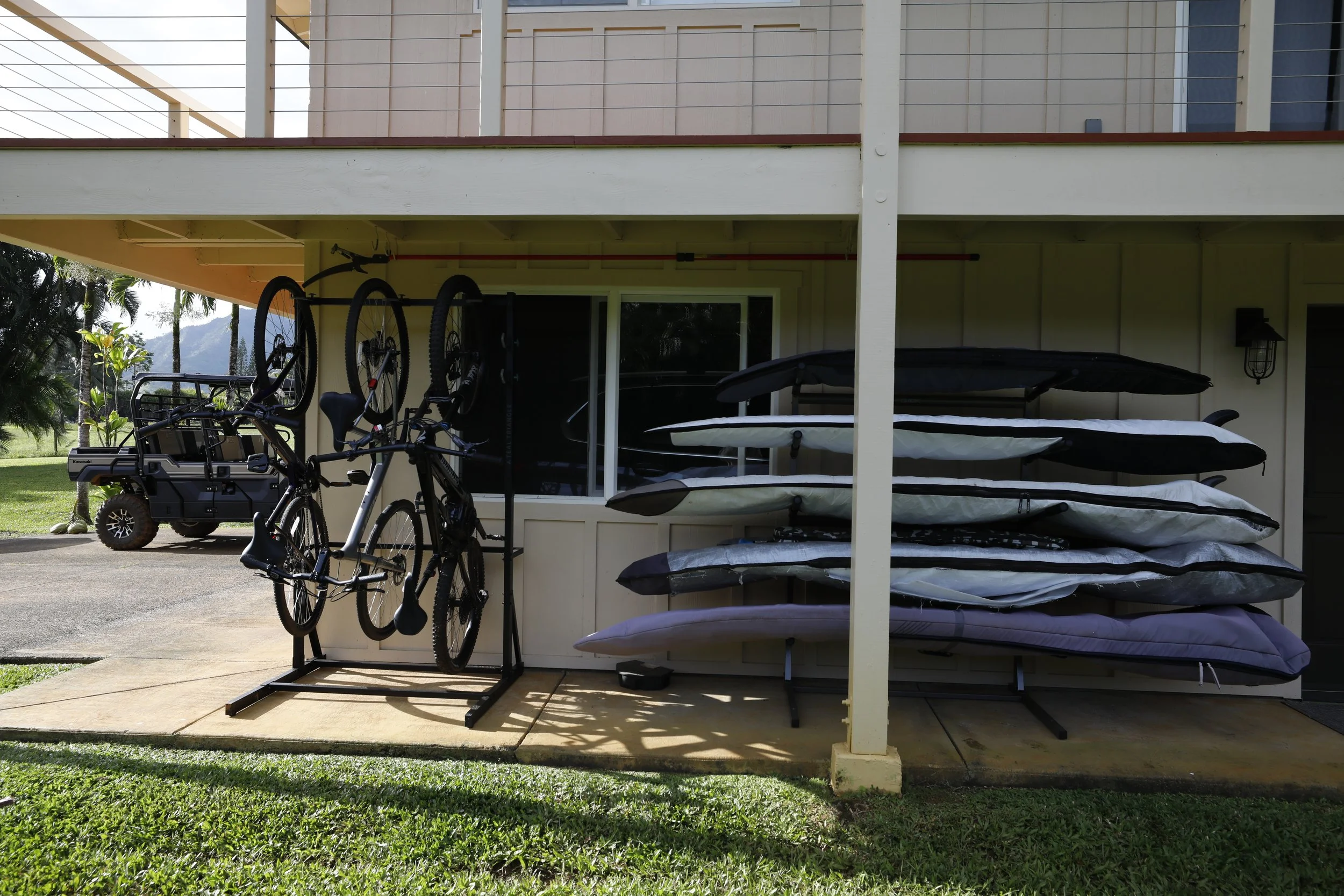 Home exterior showing stacked paddleboards, kayaks, and bikes on racks under a balcony.