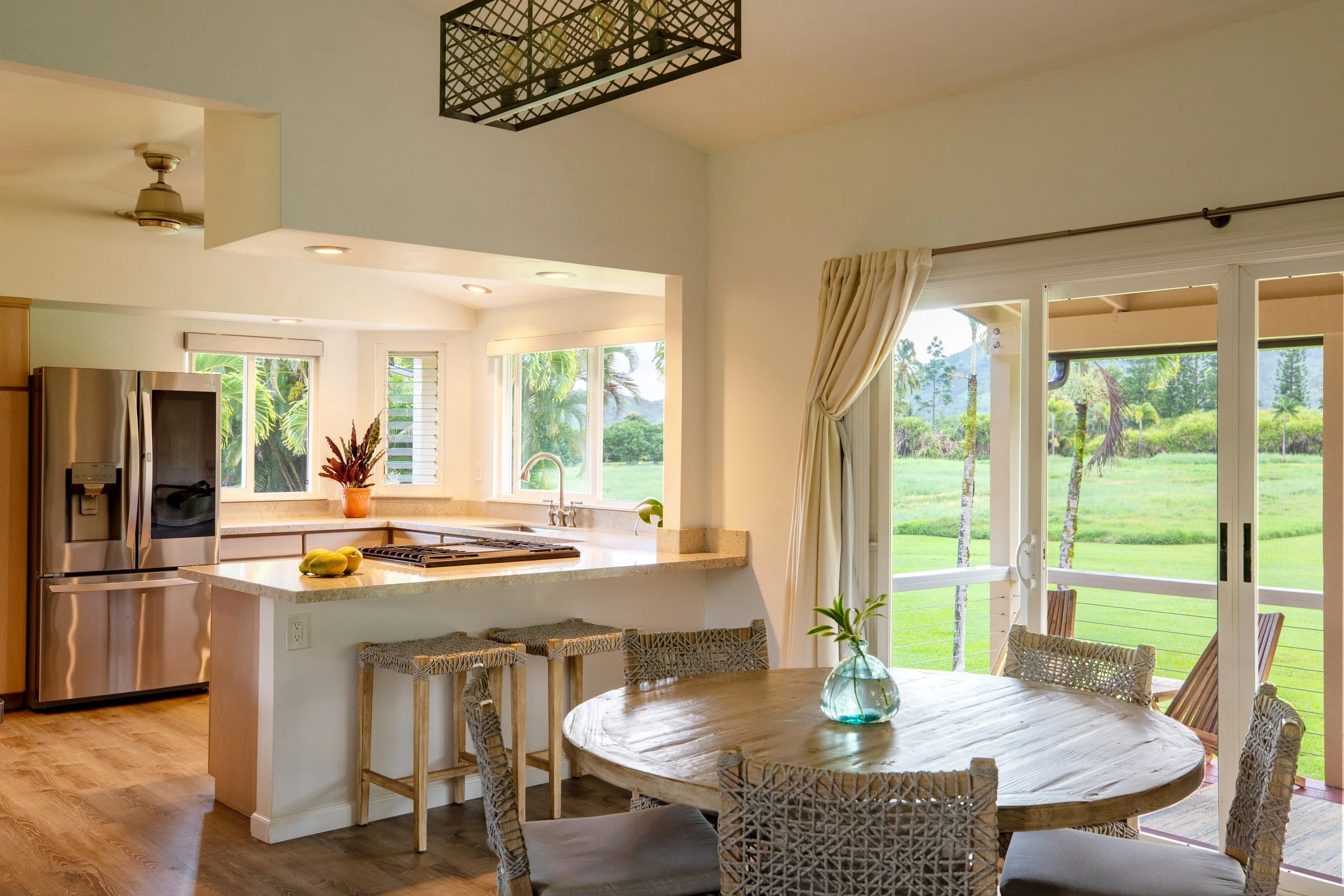 Bright kitchen and dining area with sliding glass doors leading to a green outdoor landscape, wooden furniture, and stainless steel refrigerator.