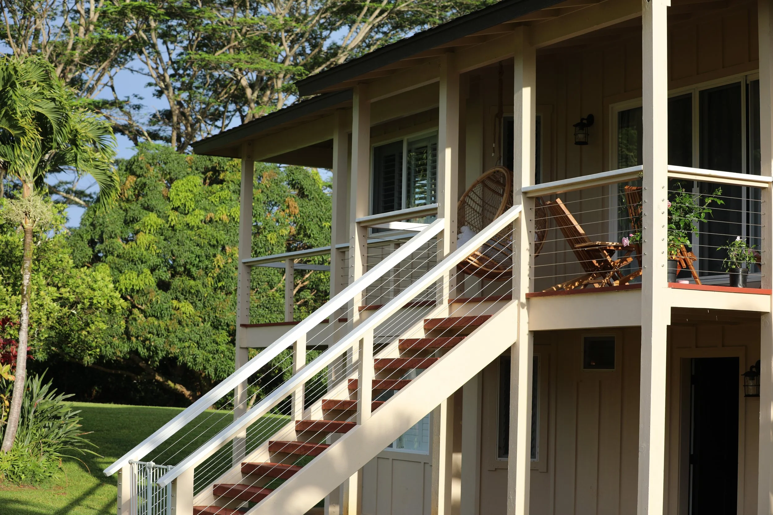Upside-down view of a house with a balcony, stairs, and outdoor furniture surrounded by trees and greenery.