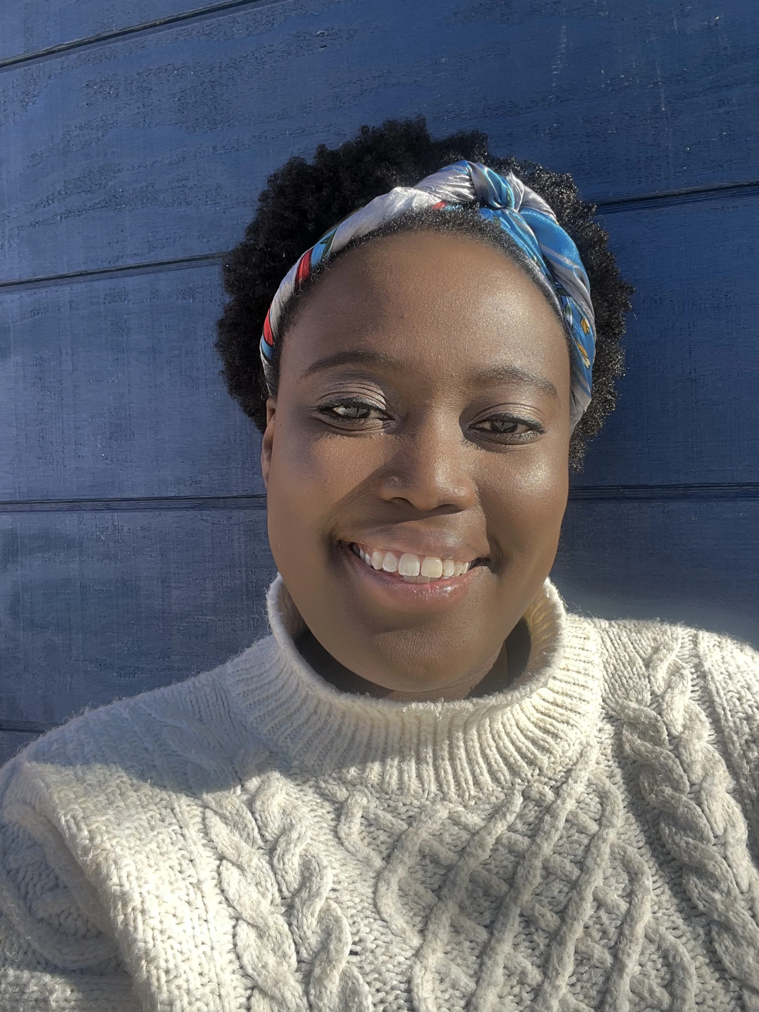 Smiling person wearing a knitted sweater and headband against a blue wooden background.