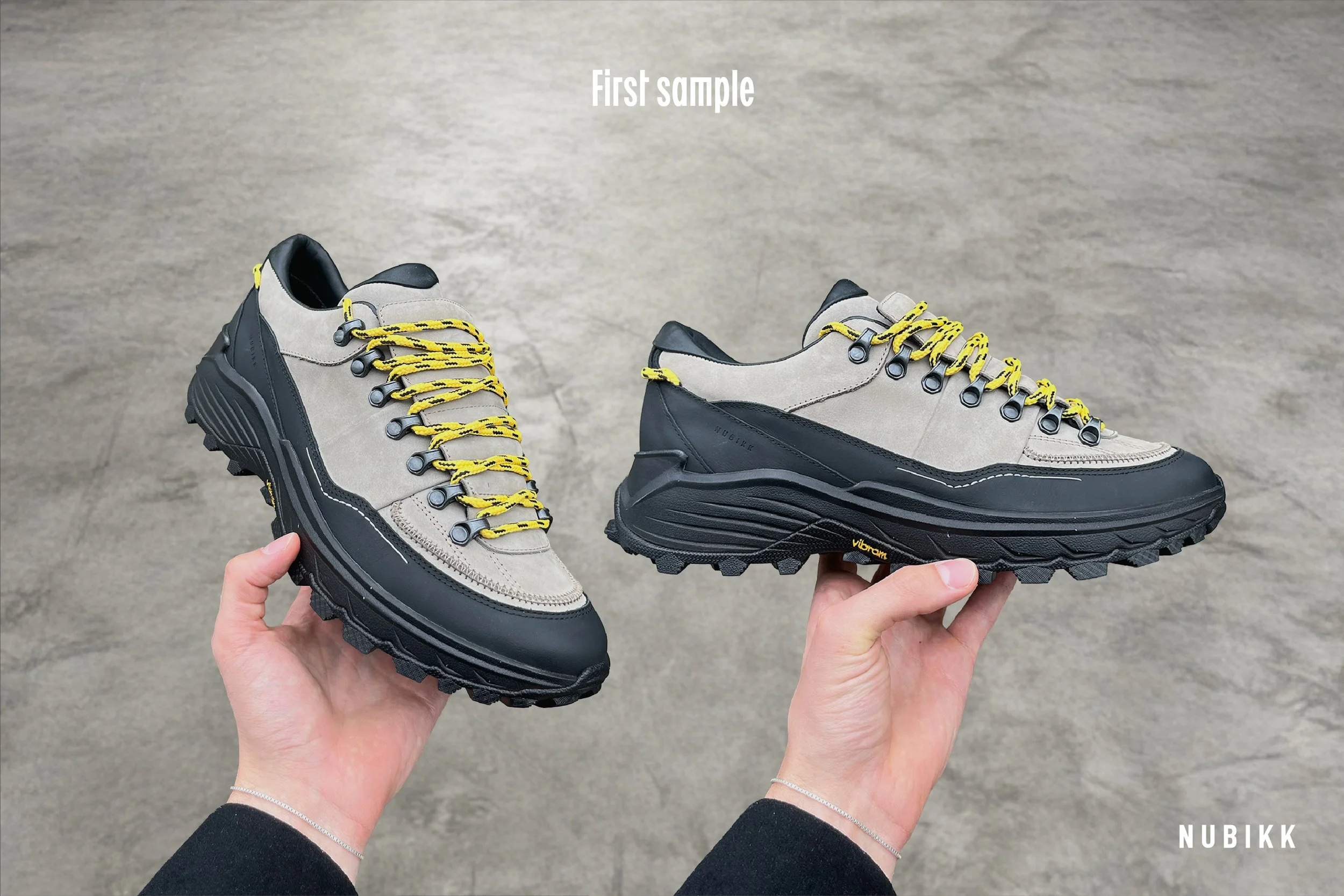 Pair of Nubikk hiking shoes with beige and black upper, yellow laces, and thick black sole.