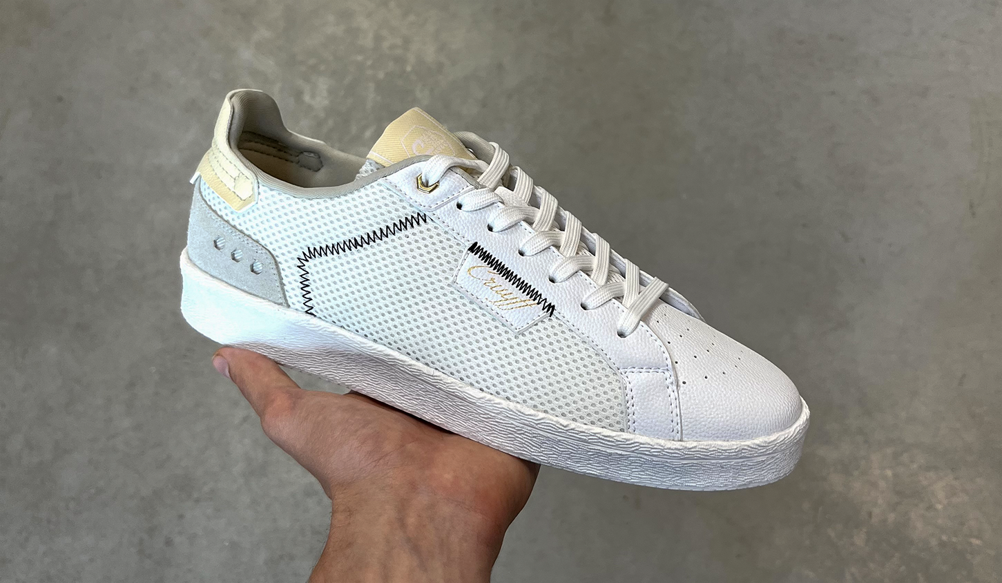 White sneaker with mesh and leather panels, being held against a gray background.