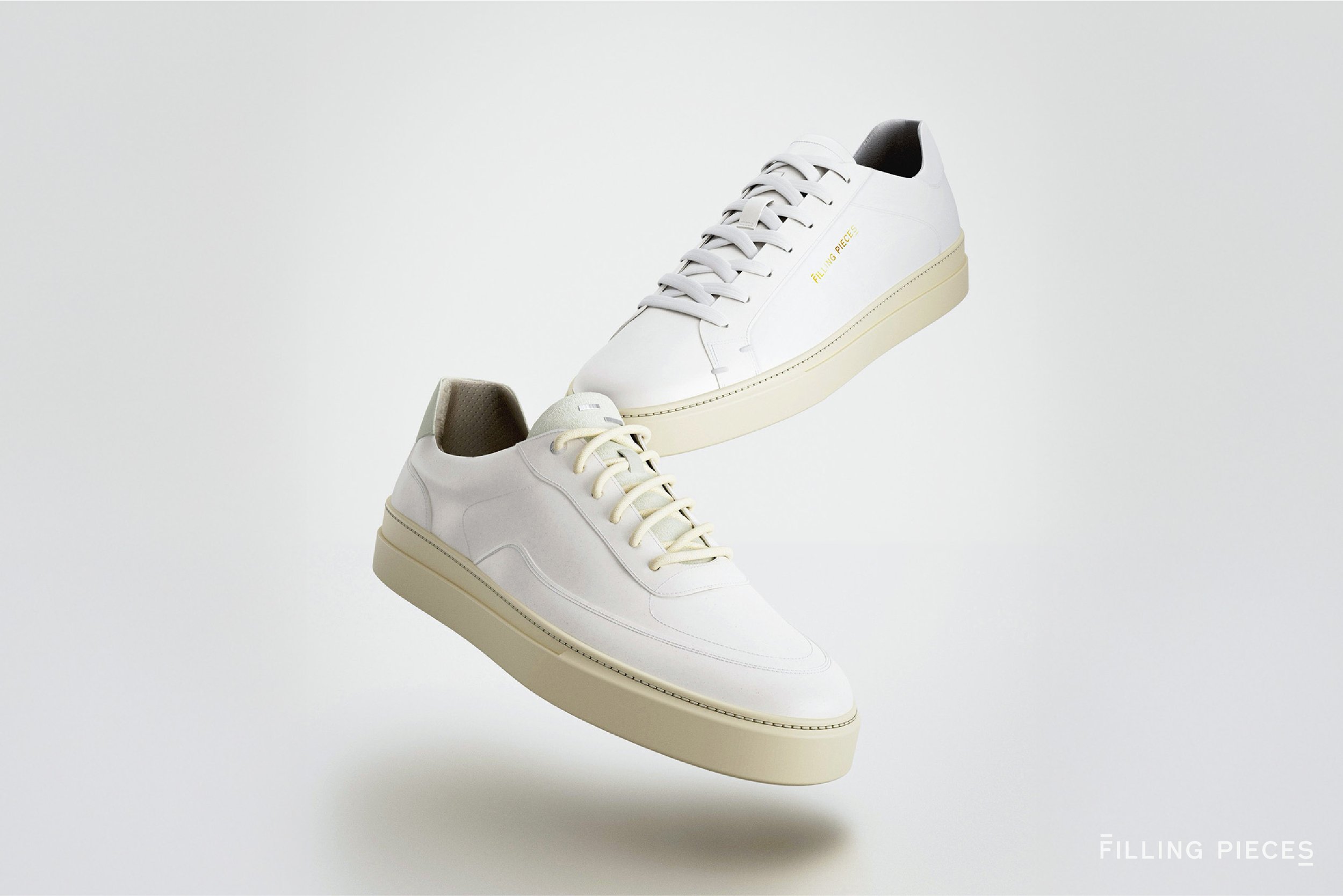 Two white sneakers, one above the other, floating against a plain background, with the name 'FILLING PIECES' in the bottom right corner.
