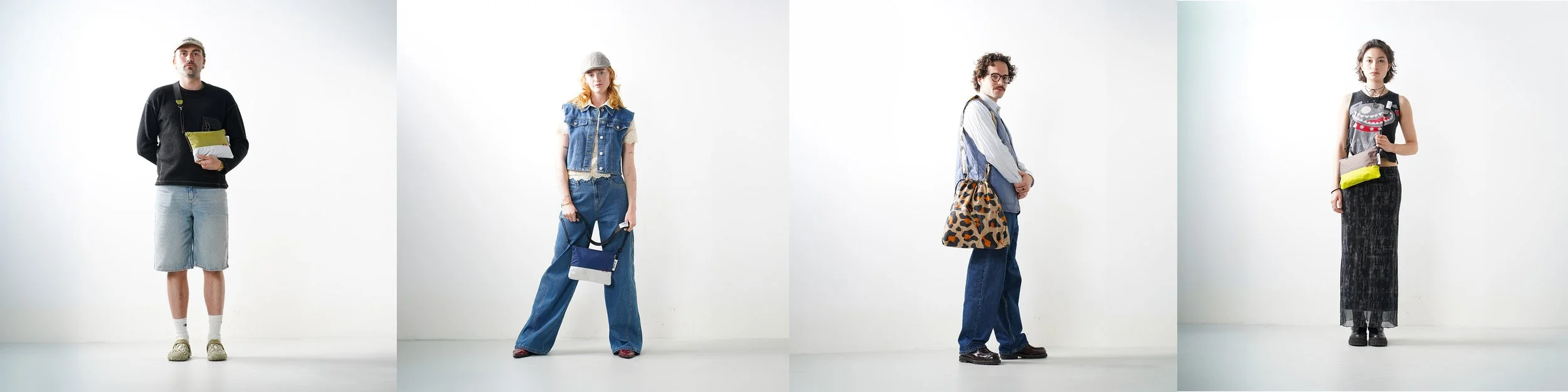 Four people standing against a plain white background, each dressed in casual, fashionable clothing and holding bags.