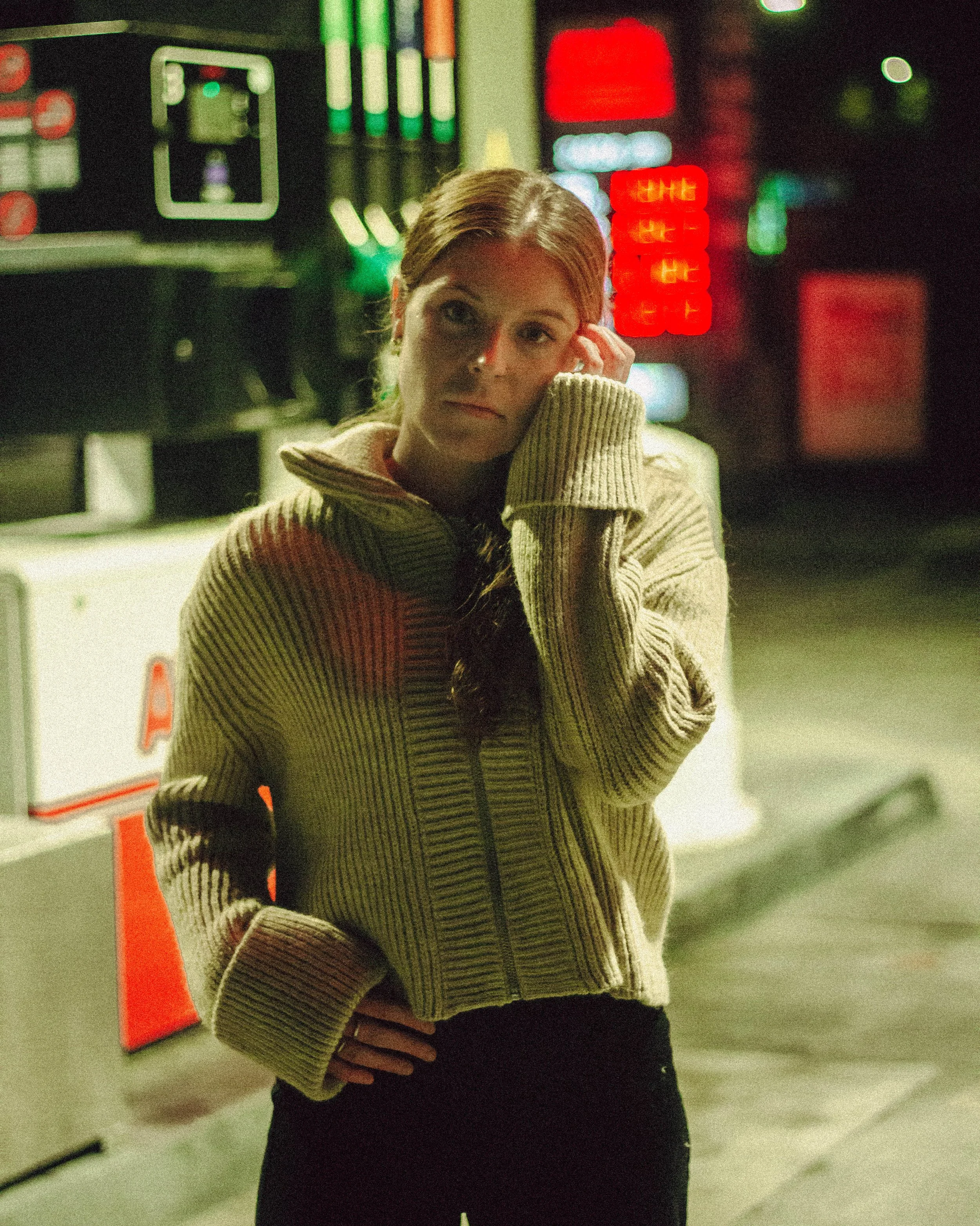 Femme avec un pull beige à une station-service la nuit.