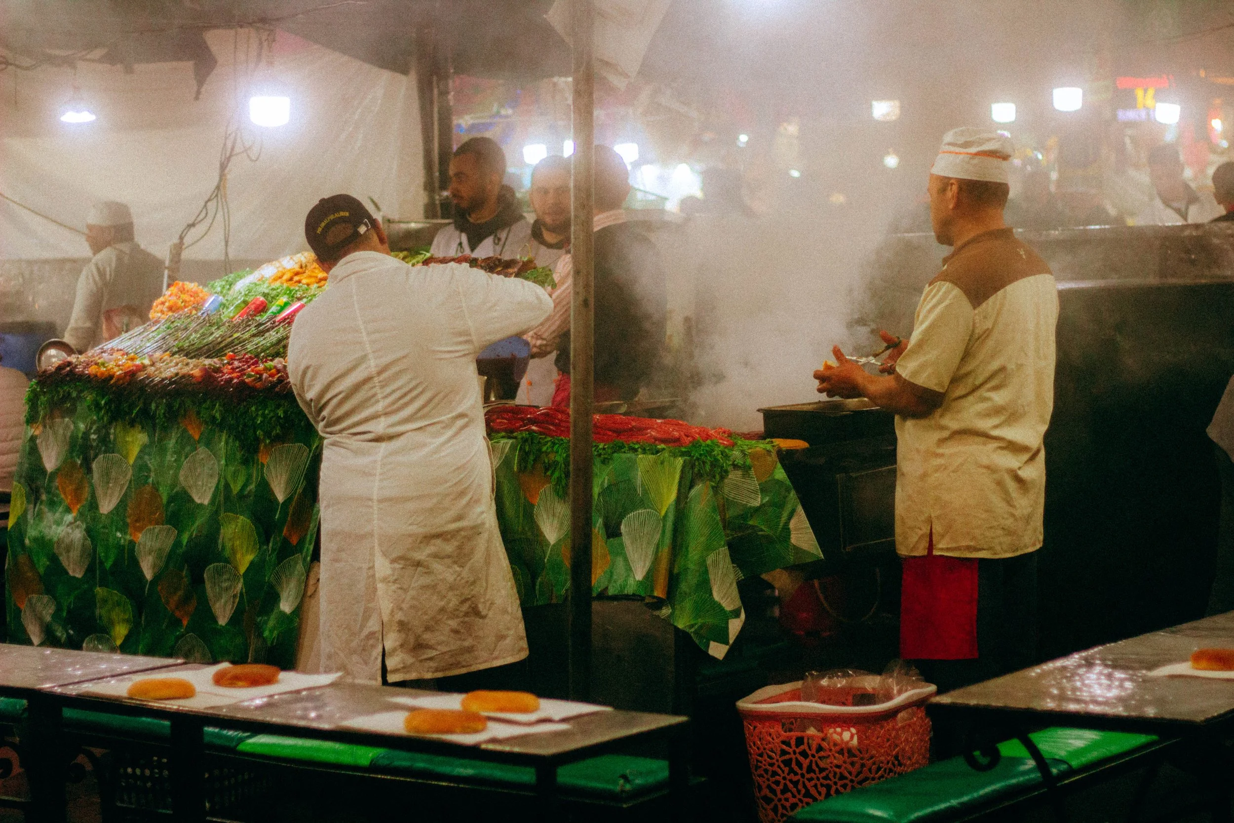 Scène de marché de nuit avec étals de nourriture et cuisiniers.