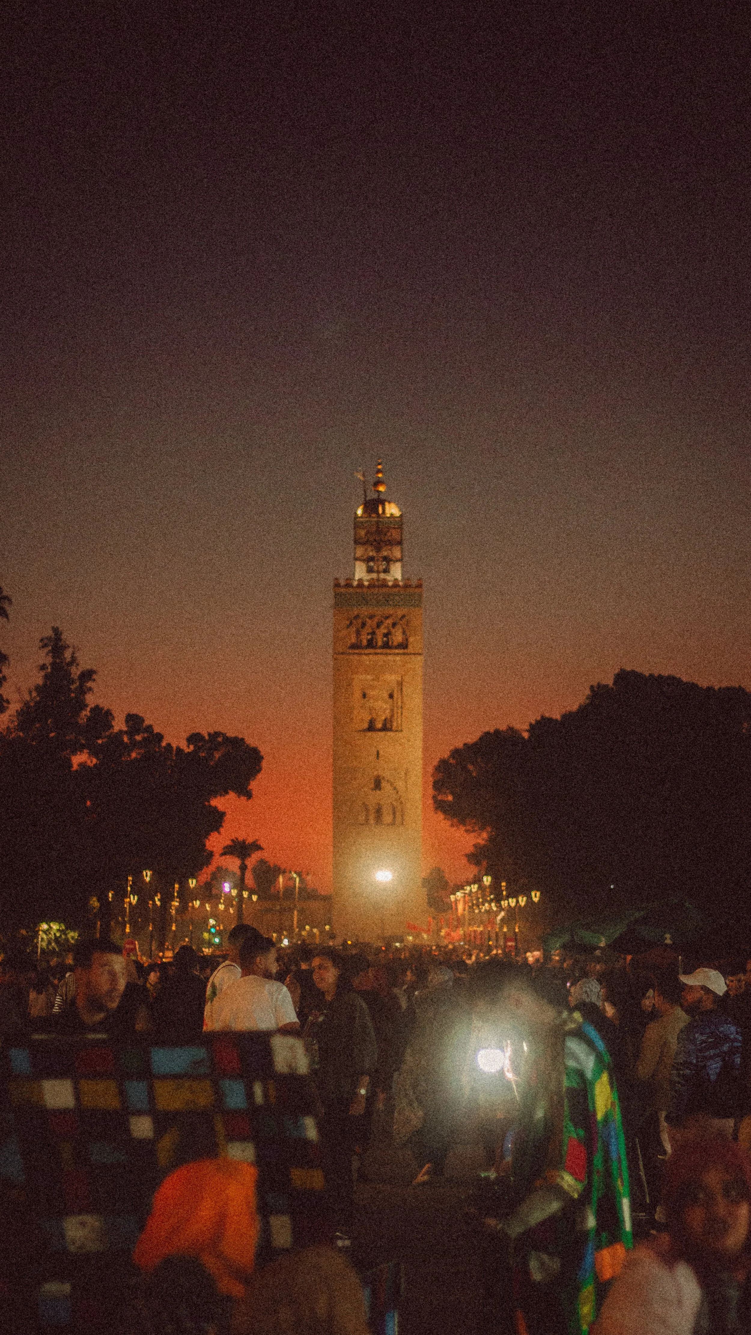 Tour de la Koutoubia à Marrakech au coucher du soleil, entourée d'une foule dans la place Jemaa el-Fna.