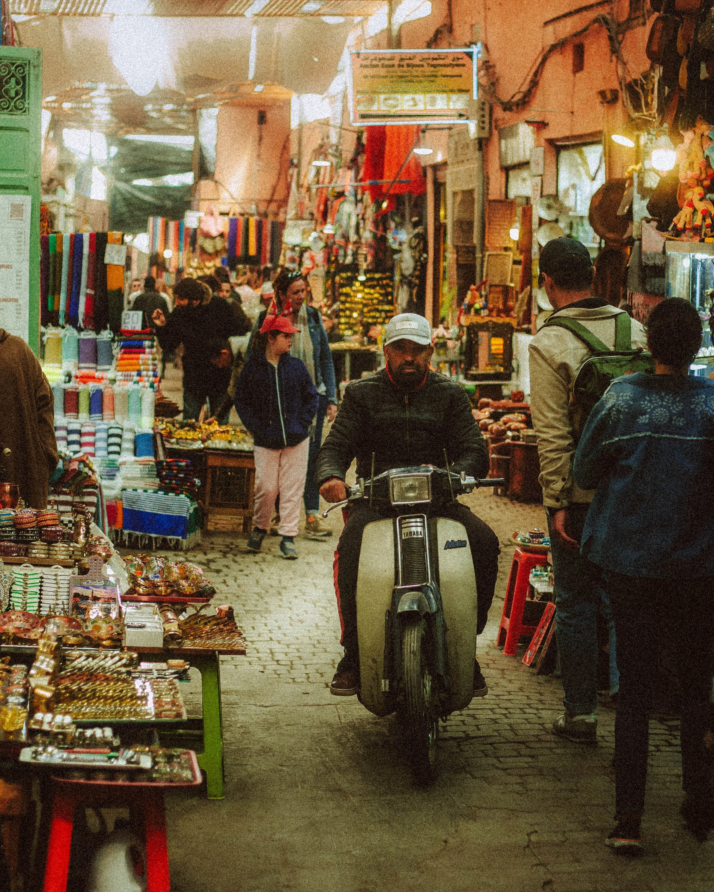 Un marché animé avec des stands de produits artisanaux et un homme sur un scooter.