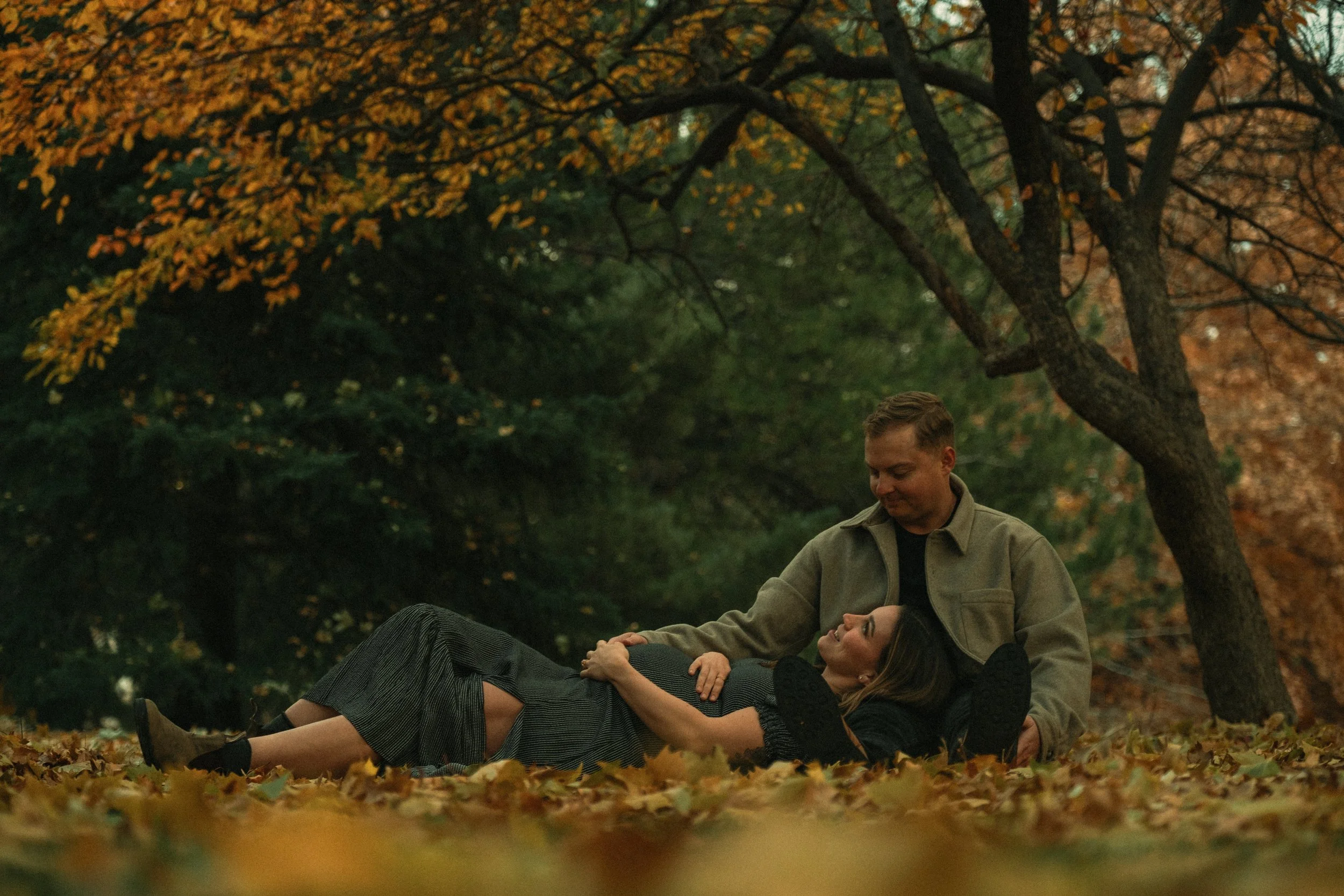 Couple sitting on autumn leaves under a tree in a park