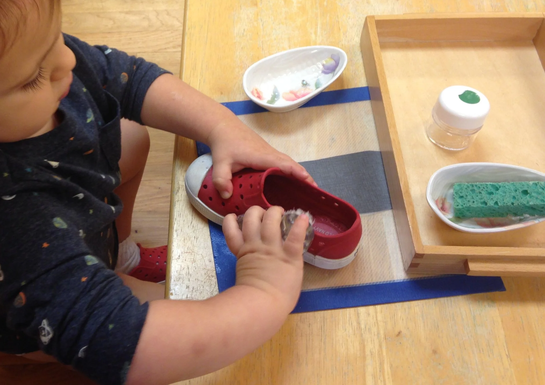 Montessori toddler washes a shoe in practical life activity at a prepared table