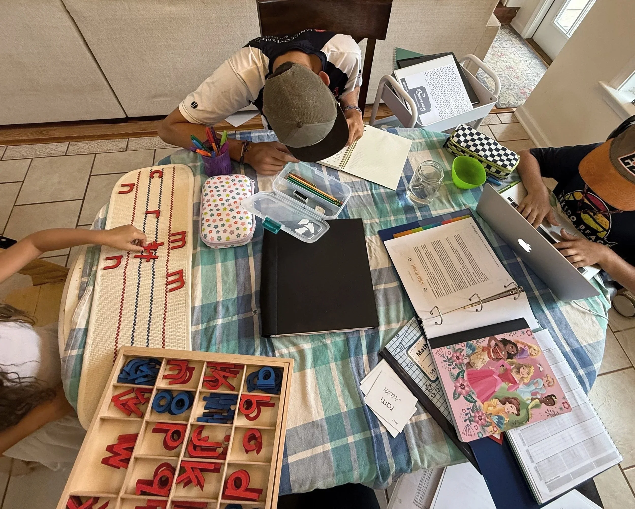 Children of mixed ages work at a table during Montessori homeschool work cycle