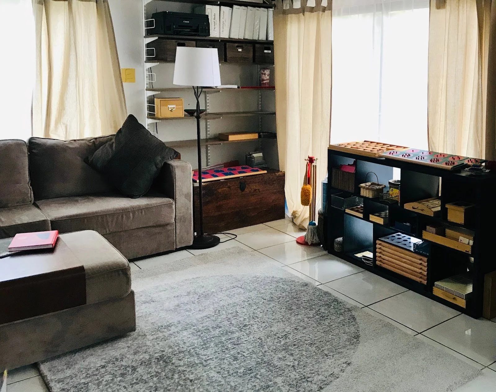 A living room is arranged to support a Montessori homeschool environment using low shelves and prepared materials.