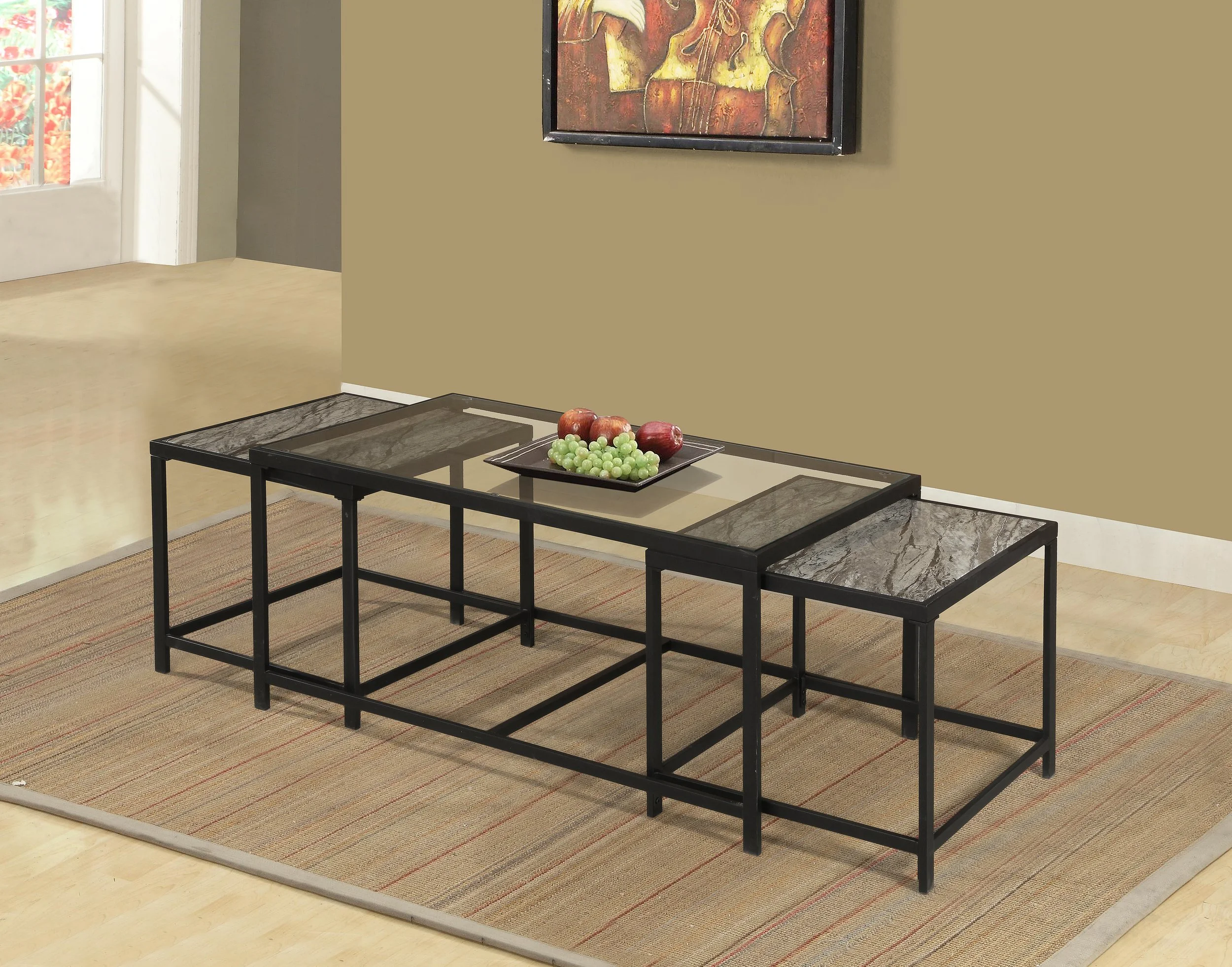 A modern black metal and glass coffee table with a centerpiece of apples and grapes on a woven area rug in a living room.