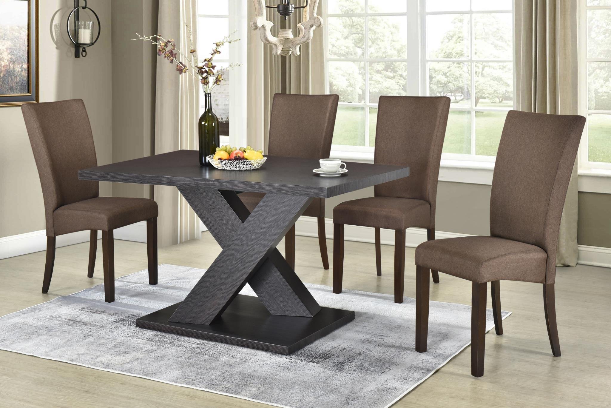 Dining room with a dark wooden table, four brown upholstered chairs, a glass vase with branches and flowers, a fruit bowl, a set of white cups, large windows with curtains, and a chandelier