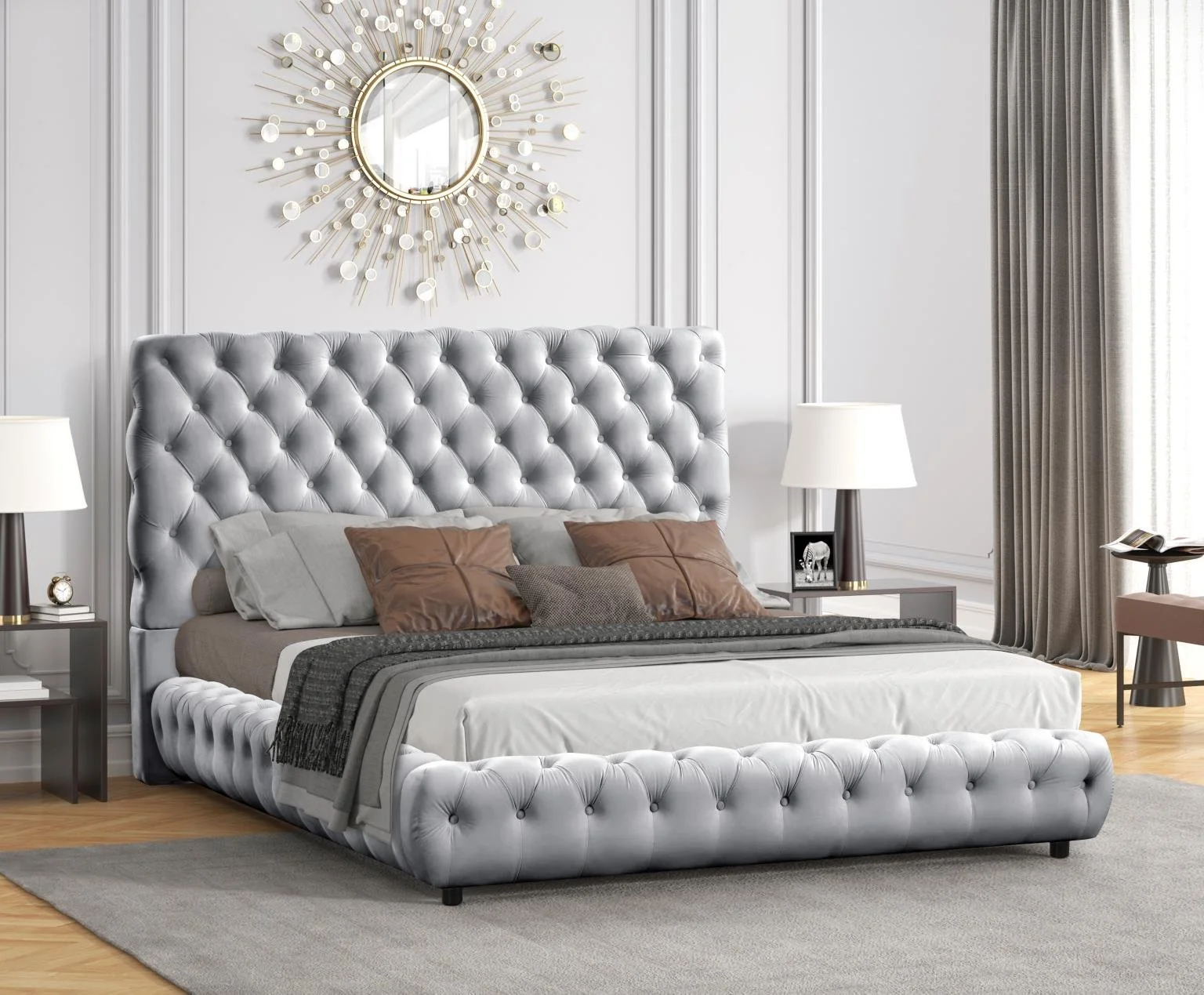 Elegant bedroom with a tufted gray upholstered bed, white bedding, several brown and gray throw pillows, gray nightstands with lamps and decor, a large round mirror with a sunburst frame on the wall, and beige curtains on a window.