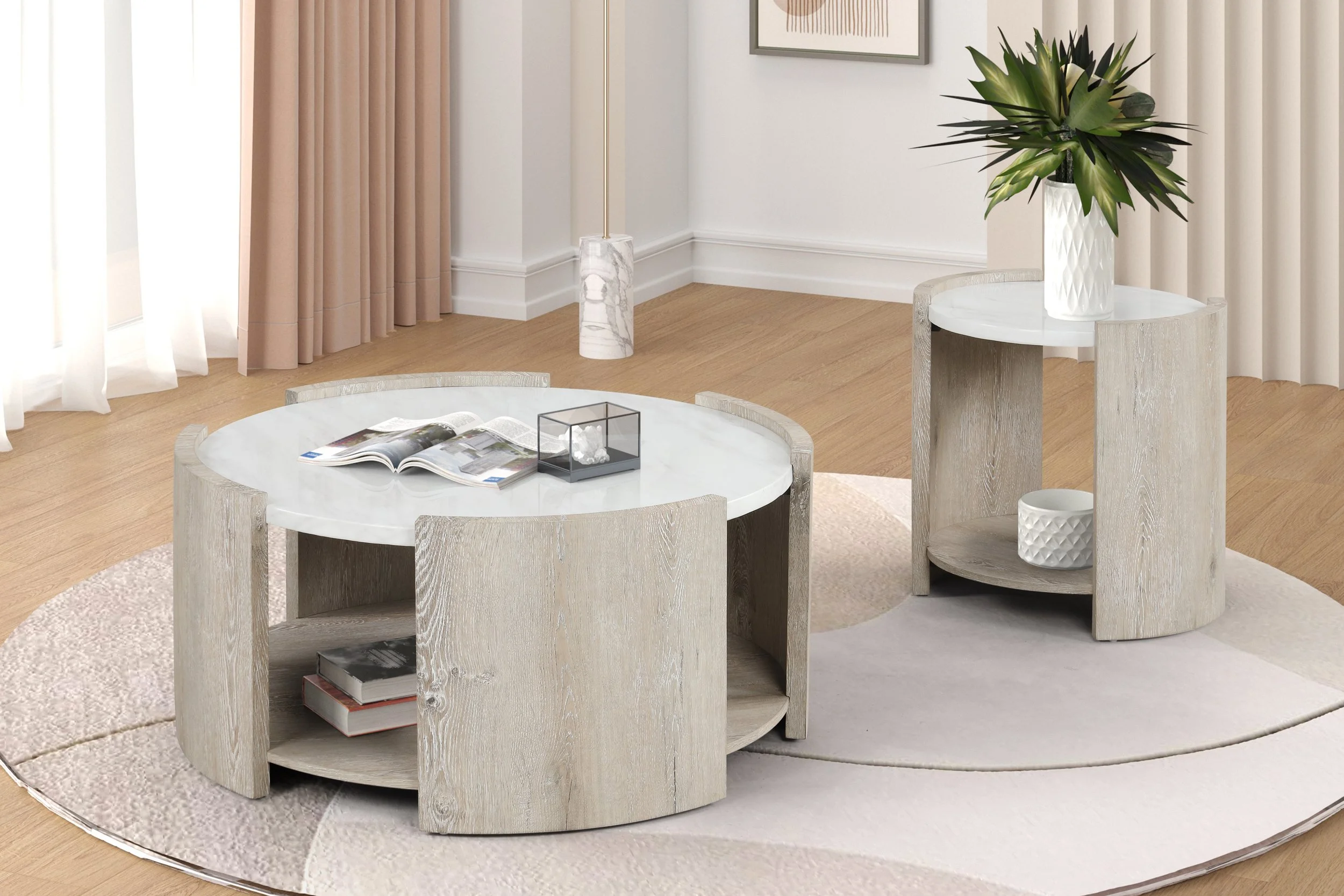 Modern living room with light wood flooring, beige curtains, and two matching round coffee tables with white marble tops and light wooden bases. The larger table has an open magazine and a glass display case with a white decorative item, while the smaller table has a plant in a white textured vase and a white textured bowl. There is a framed artwork on the wall, a floor lamp with a marble base, and a circular area rug underneath the tables.