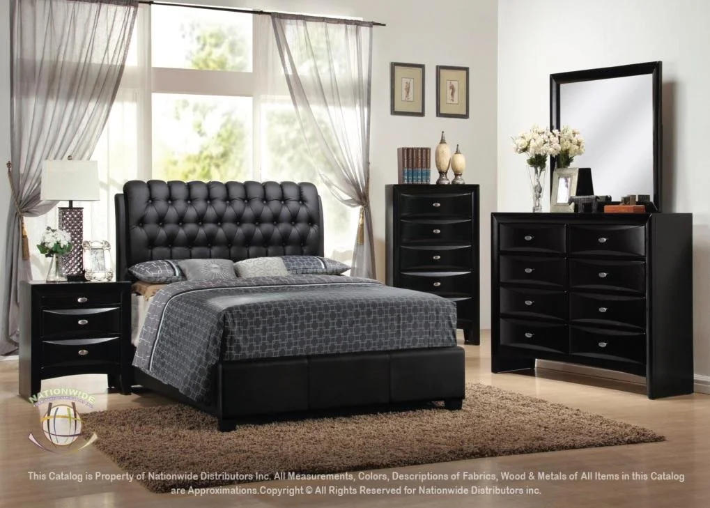 A bedroom with a black tufted headboard and matching black furniture, including two nightstands, a tall dresser, and a six-drawer dresser with a mirror, decorated with a vase of white flowers, framed pictures, and books, in front of large windows with curtains.
