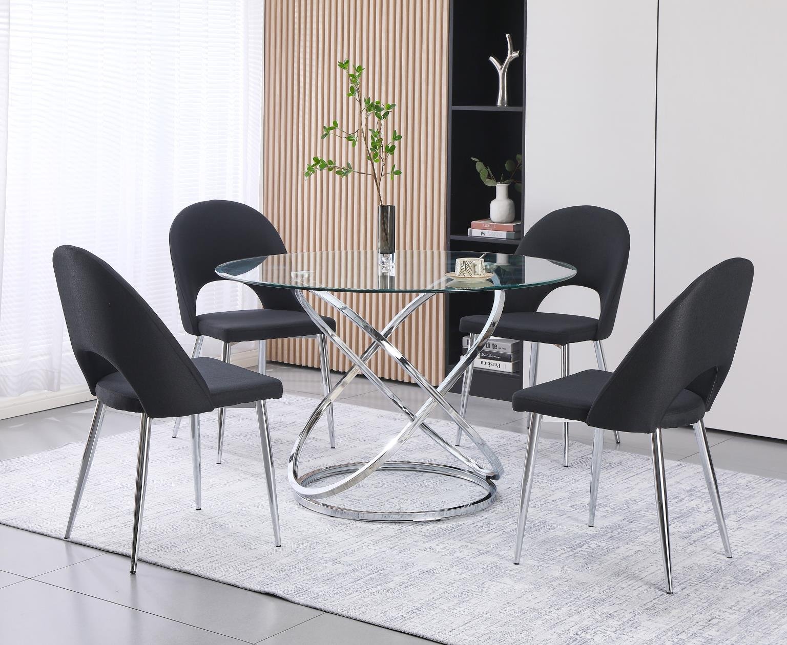 Modern dining room with a round glass table and five black chairs, a white rug, a wooden wall with a plant in a vase, and built-in shelves with decorative items.