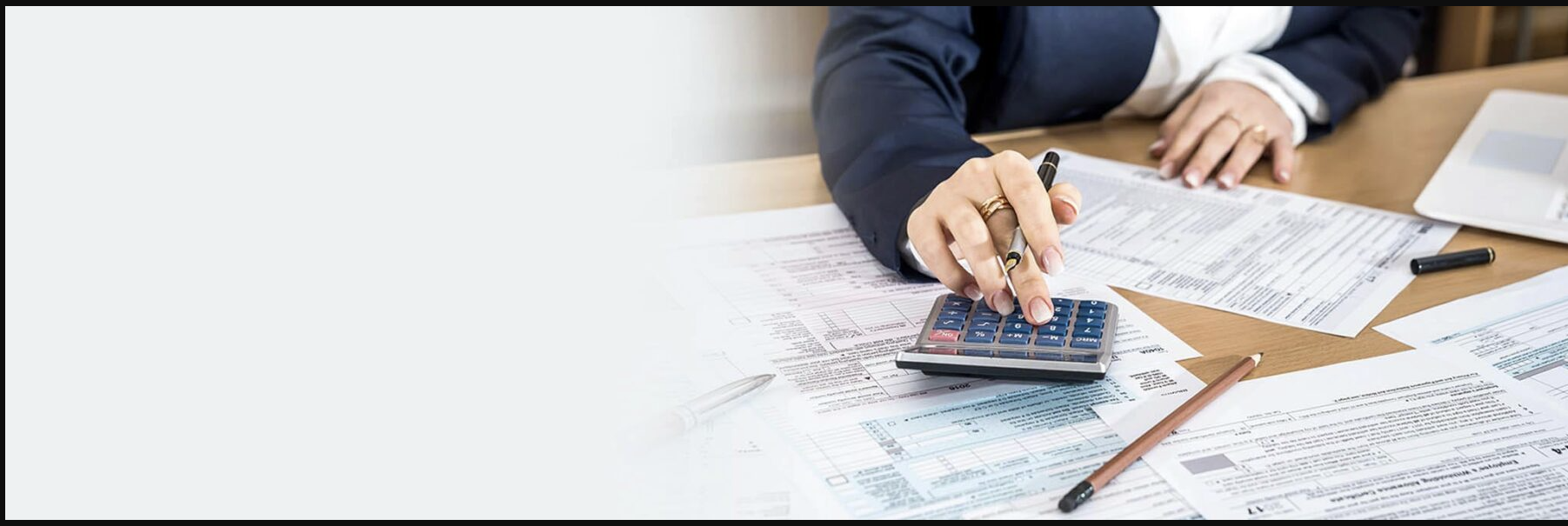 Person in business attire using a calculator and pen on financial documents on a desk.