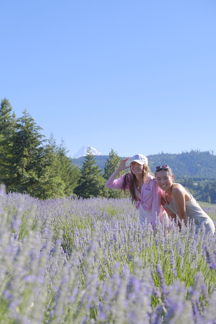 Jungyeon and Kristie are wearing summery outfits smiling at the camera in a lavender field.