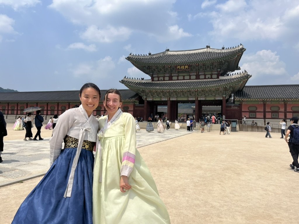Kristie and Jungyeon pose in front of a Korean historical landmark palace, wearing Korean traditional dresses.