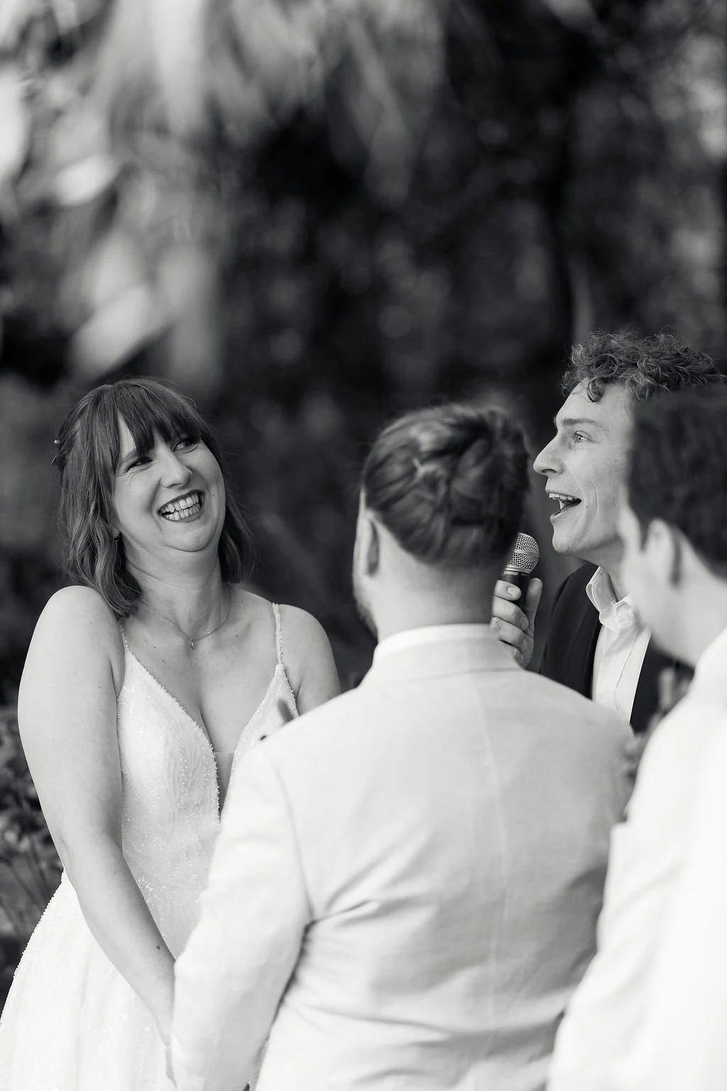 Standing in front of the gorgeous harbour with a floral arrangement sitting behind the couple as Stan marries them, the couple holds hands in between them  