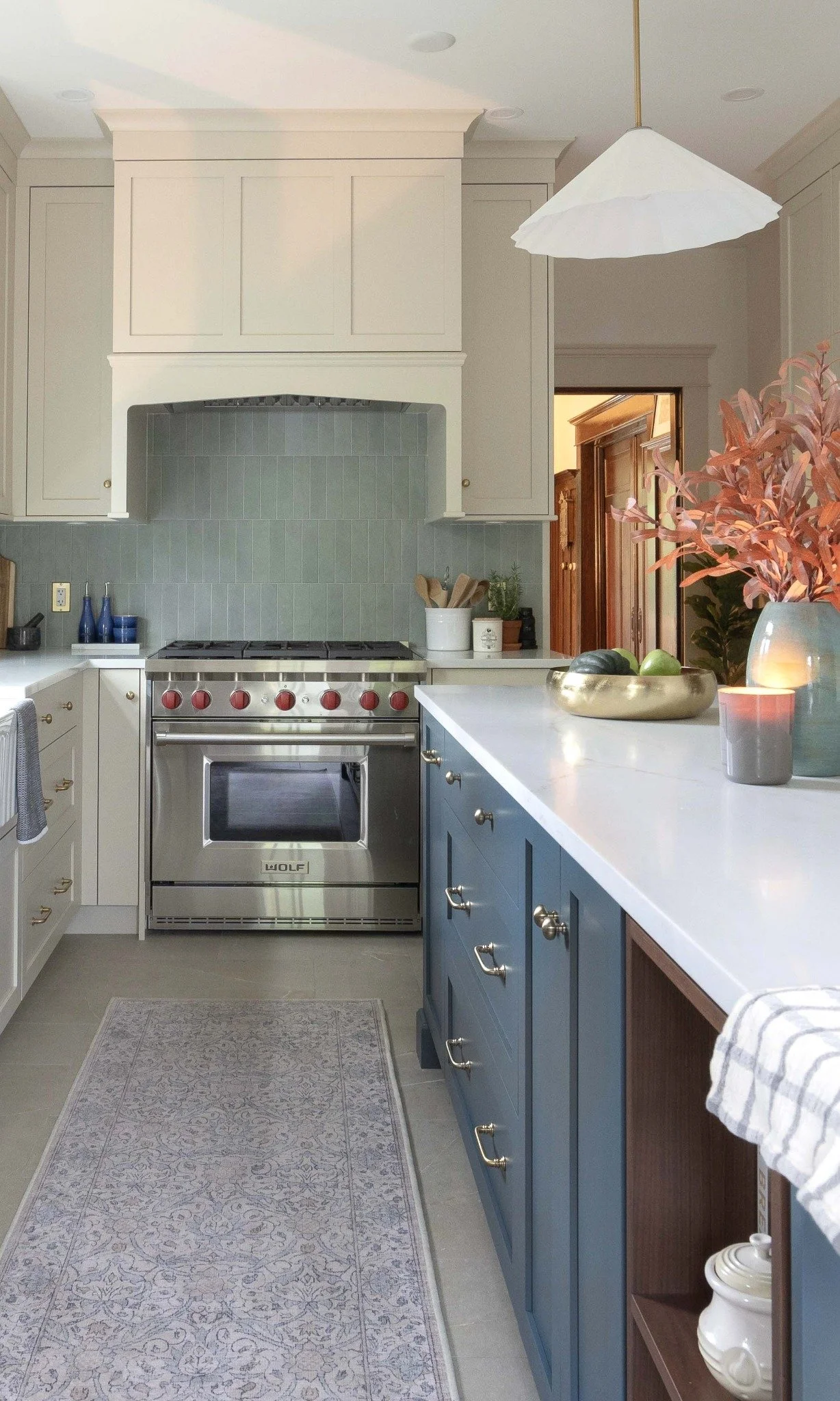 A Langley kitchen with a white range and hood, teal backsplash, white countertops, blue cabinets with gold handles, and decorative items including a bowl of fruit, vases, and candles.