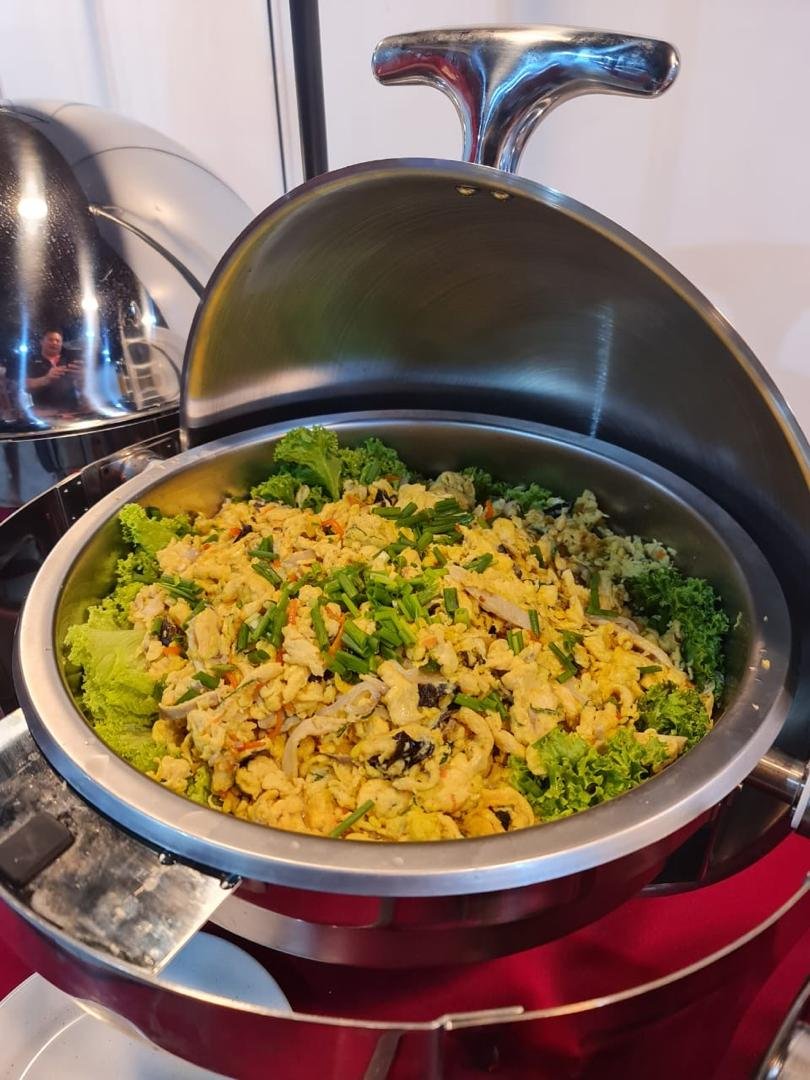 Buffet dish with scrambled eggs and vegetables in a stainless steel chafing dish.