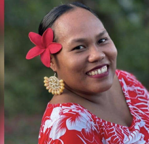 Woman with a red flower in her hair, wearing a red and white floral dress, smiling outdoors.