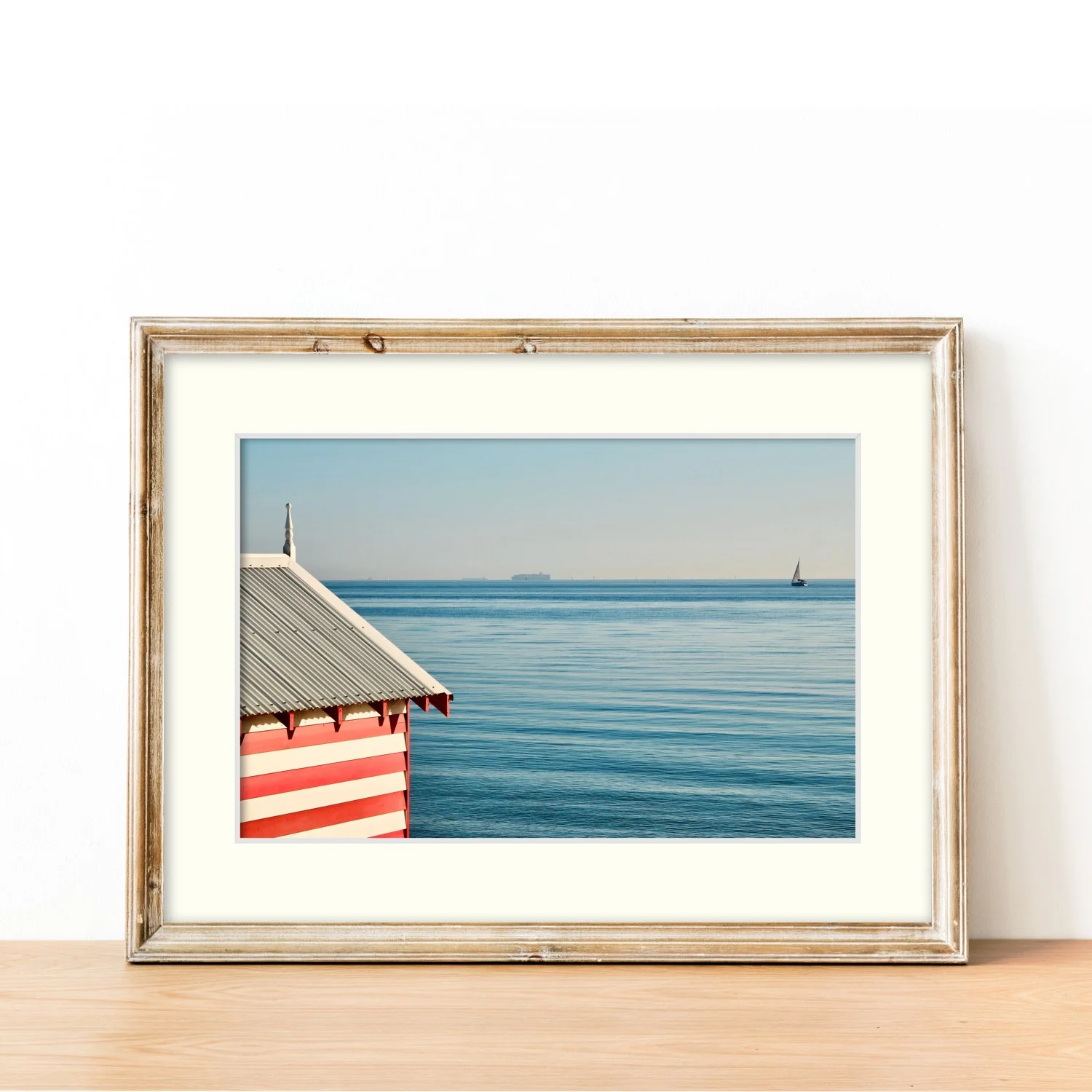 Frame mount with print of red and white bathing box against vivid blue waters in finalised picture frame on sideboard.